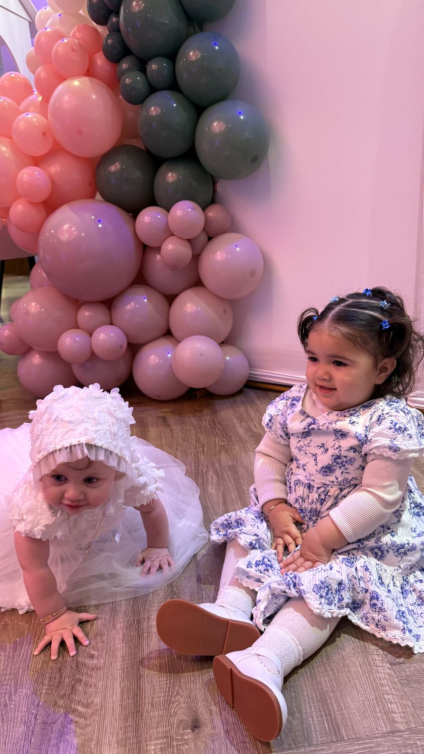Two toddlers sitting in front of a pastel balloon garland