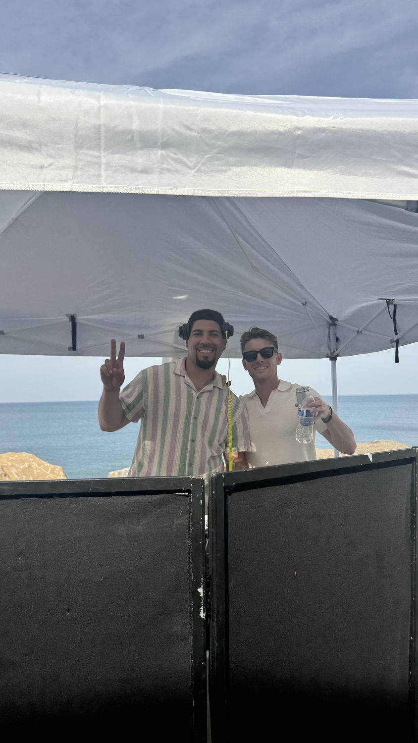 Two DJs under a tent behind a black facade