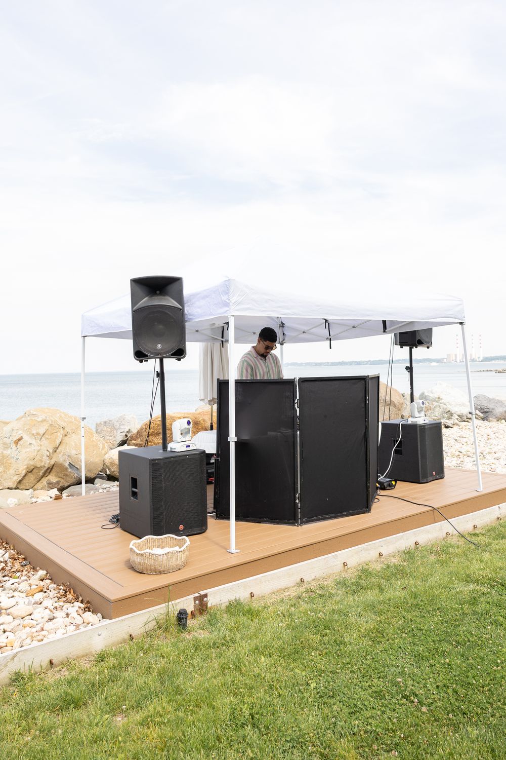 Speakers and DJ setup under a white tent at a waterfront event